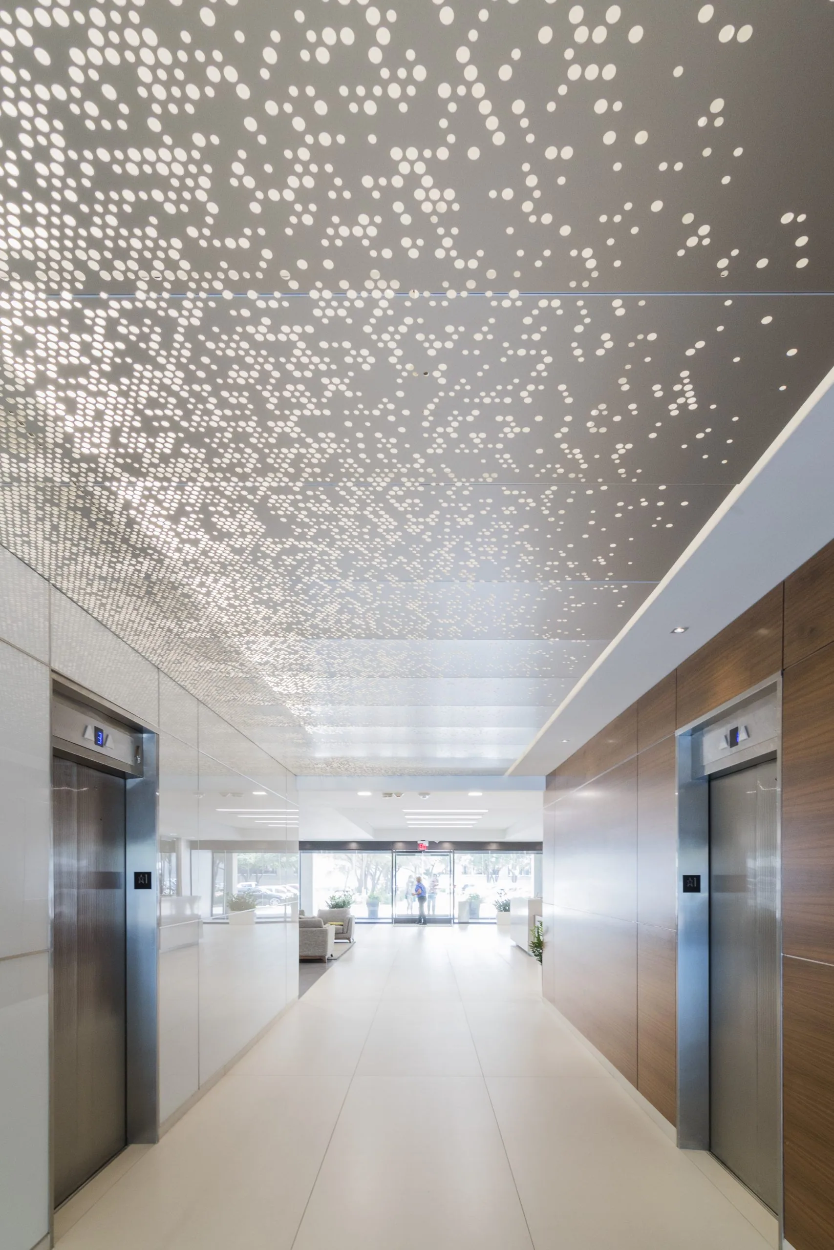 A perforated ceiling glowing over an elevator lobby