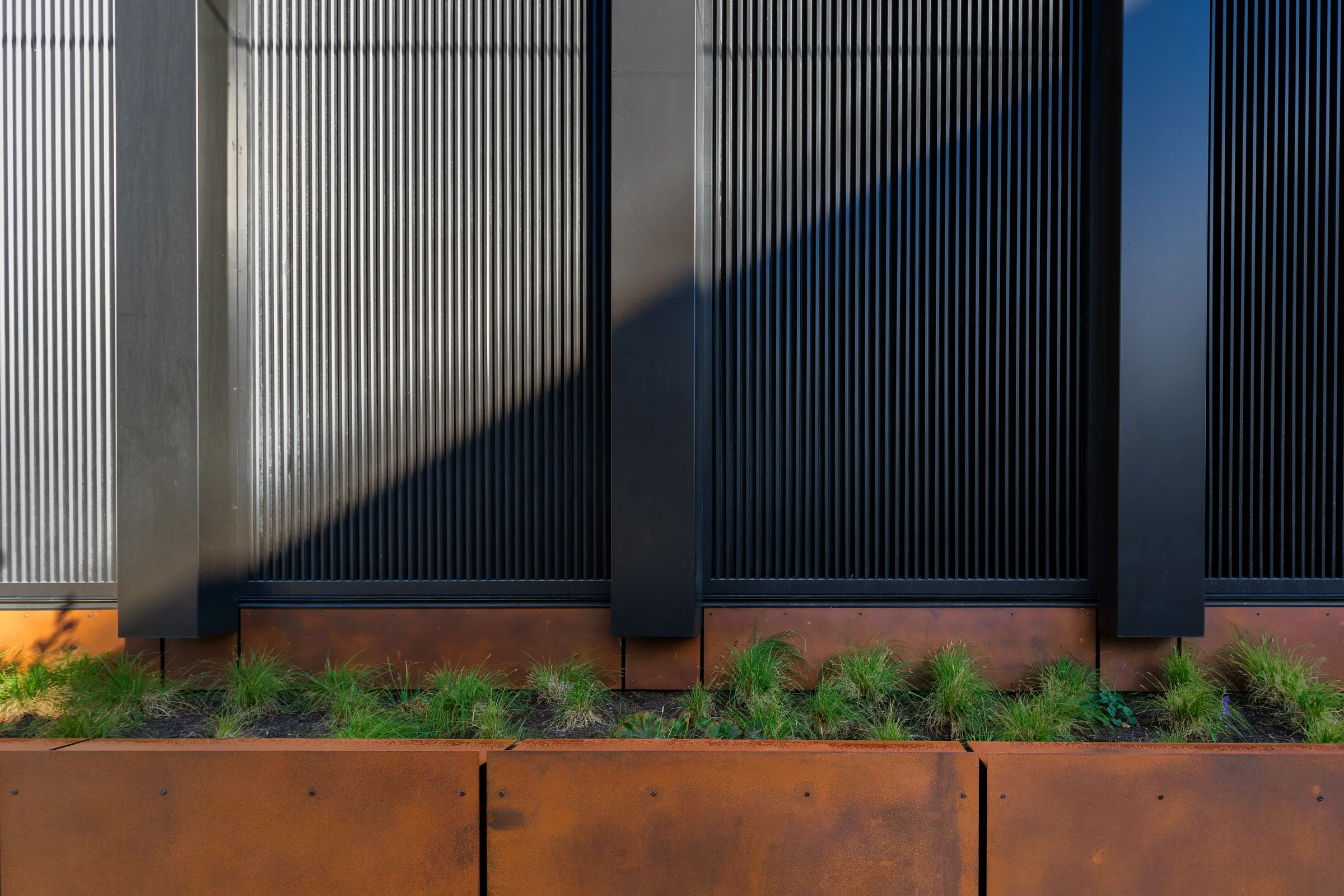 A steel planter wall along a black-ribbed façade
