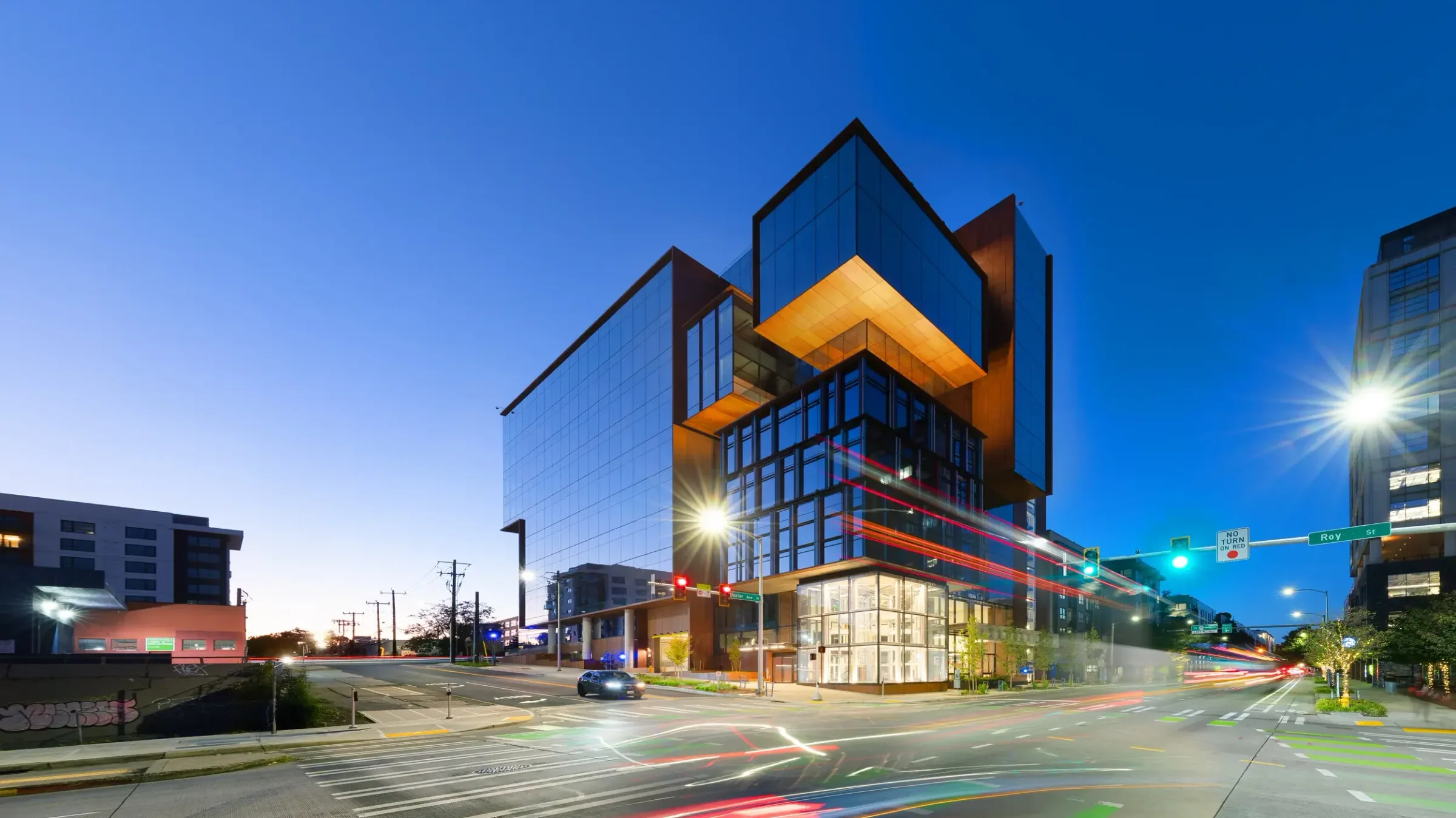 The building at dusk, car lights streaking past