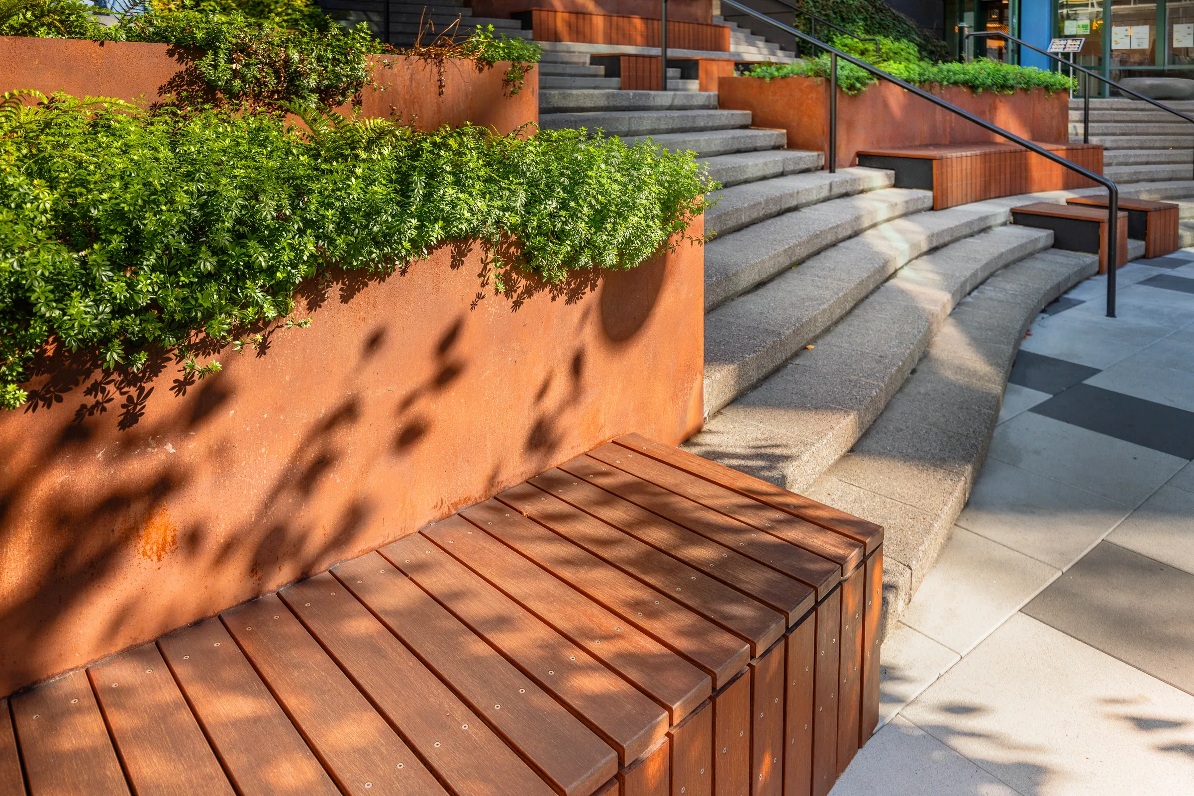 A curved wood bench in a steel planter, sun on the steps