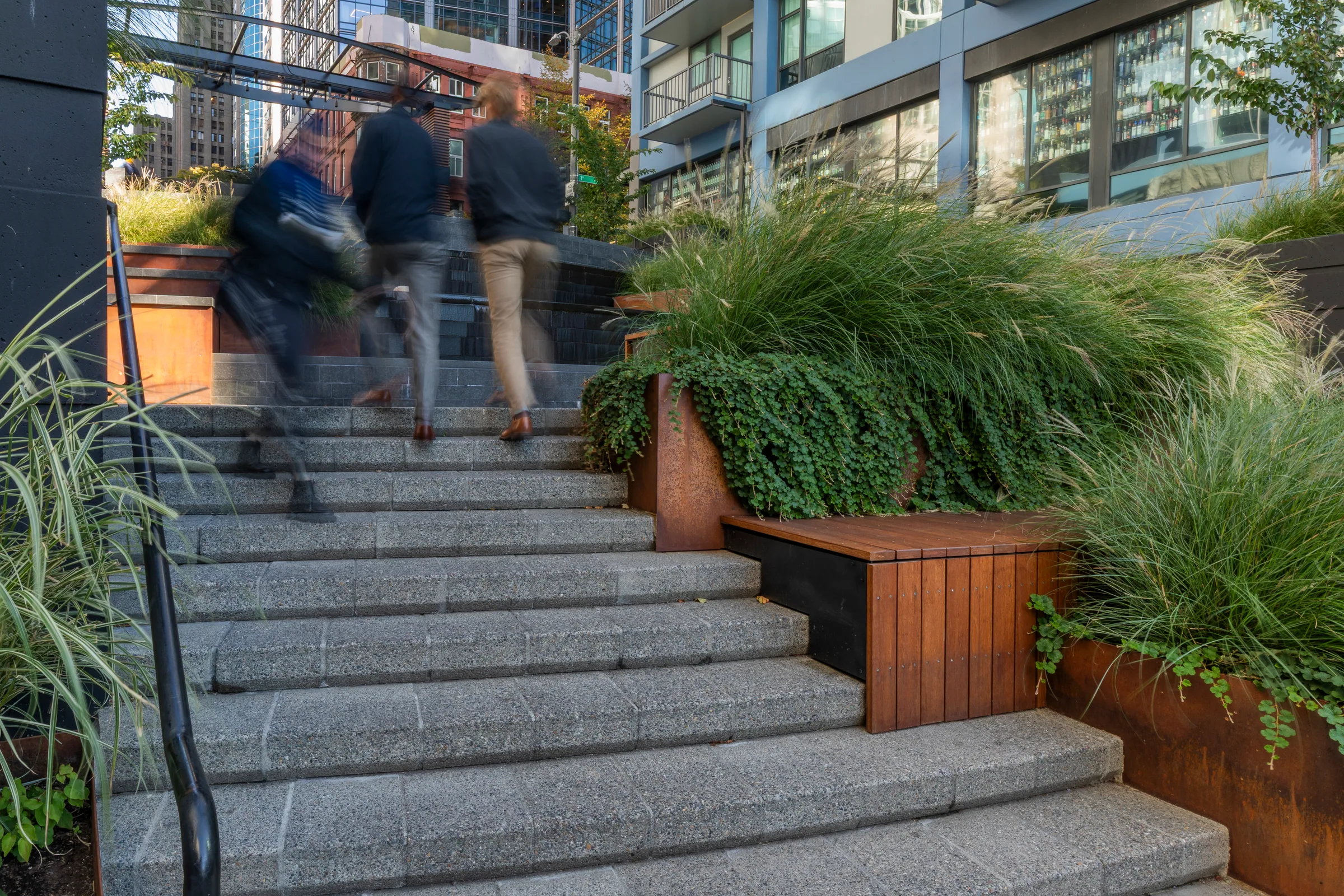People climbing the steps past steel planters and grasses