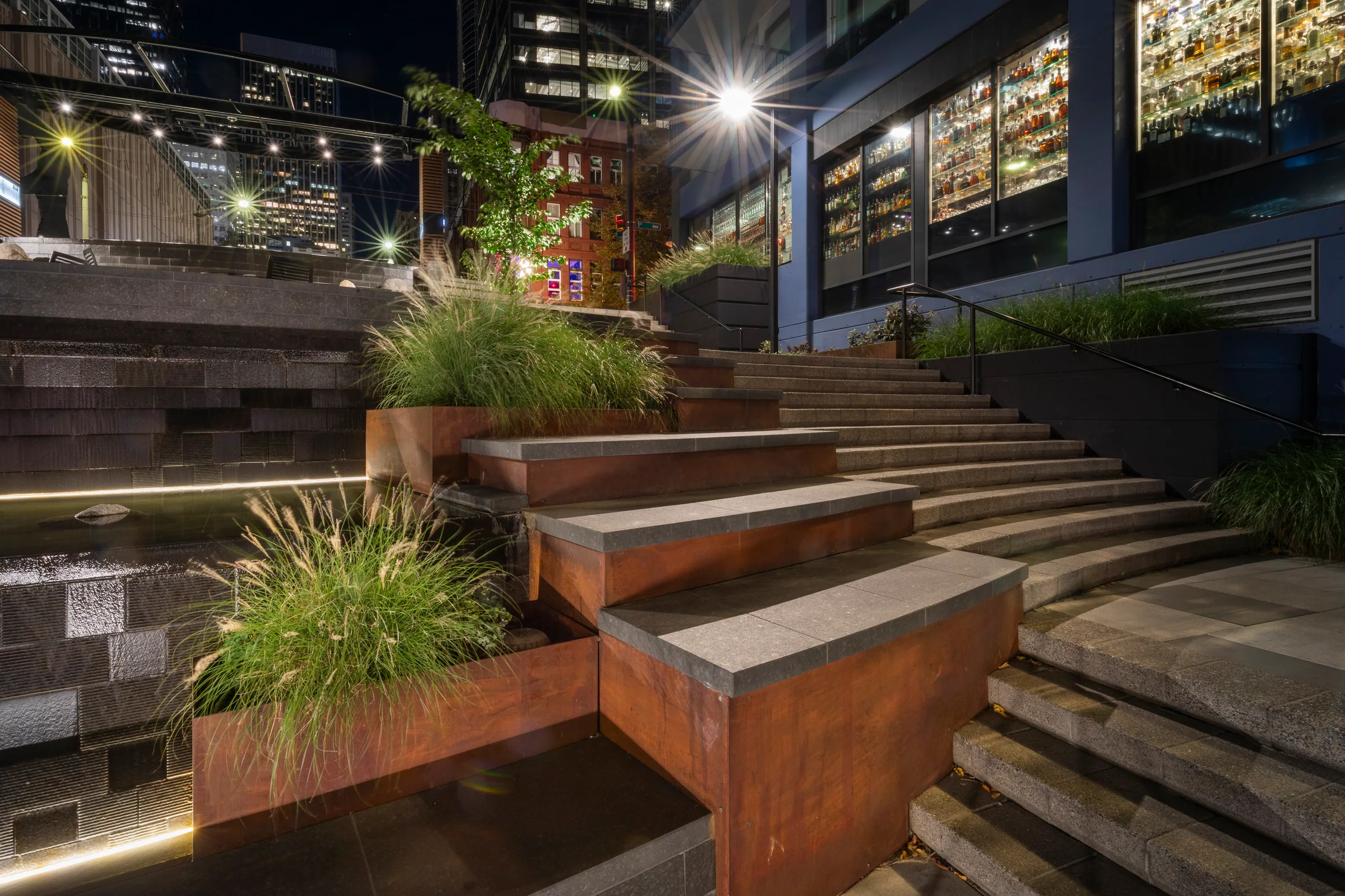 A lit steel planter and fountain at night