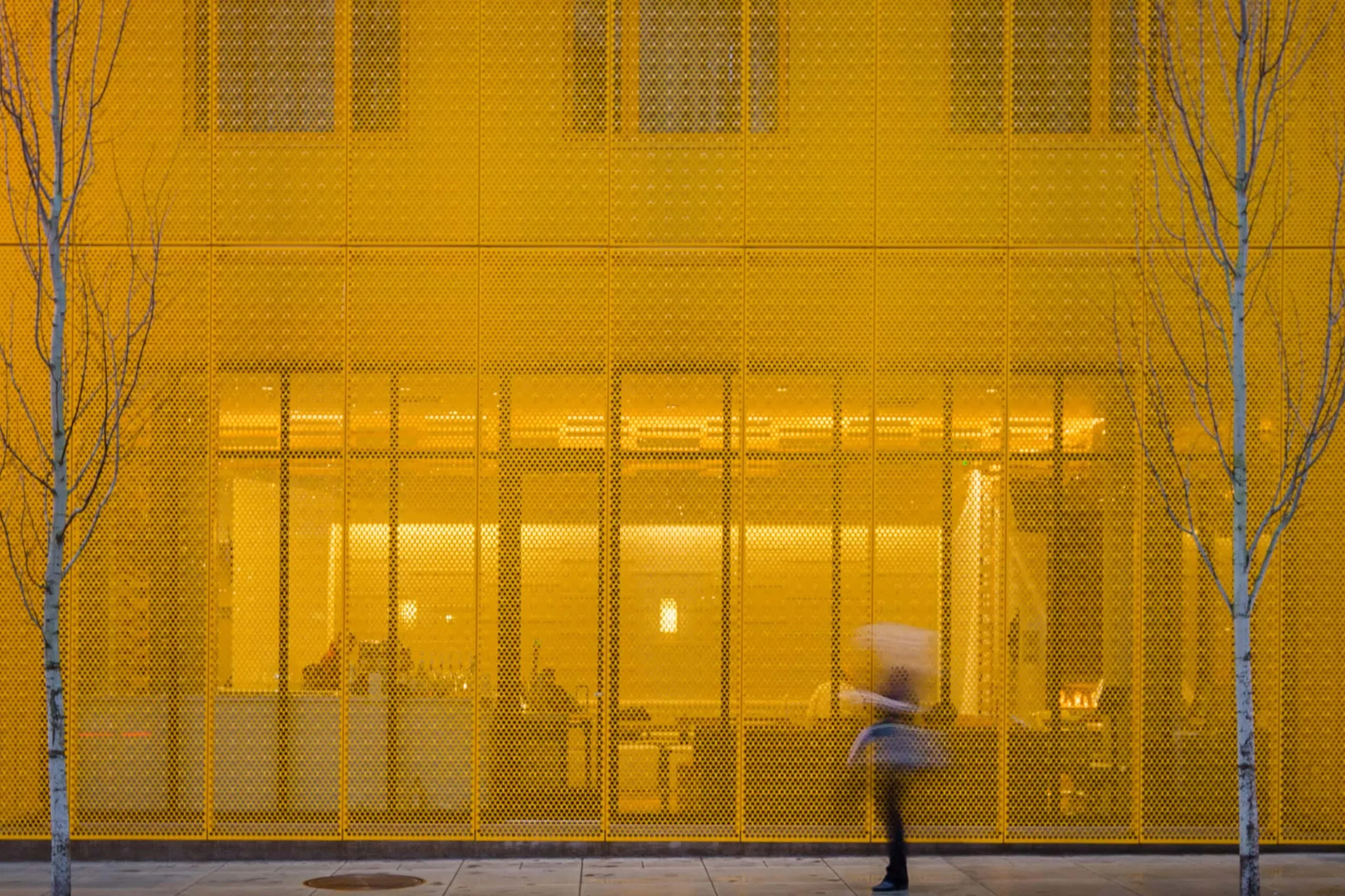 Straight on to the yellow screen and the lit lobby behind it, a passerby blurred in motion