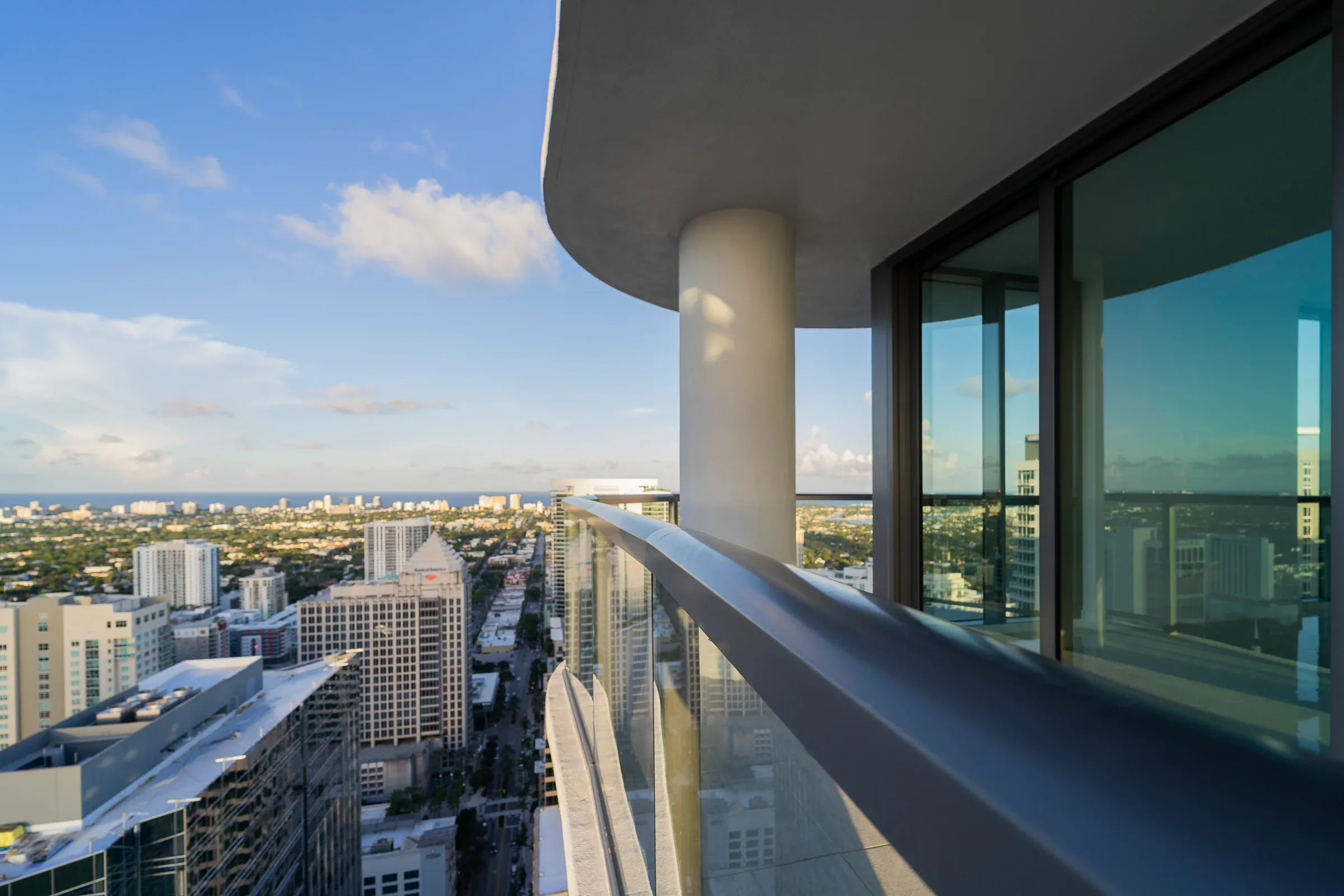 A balcony’s glass railing and round column against the sky