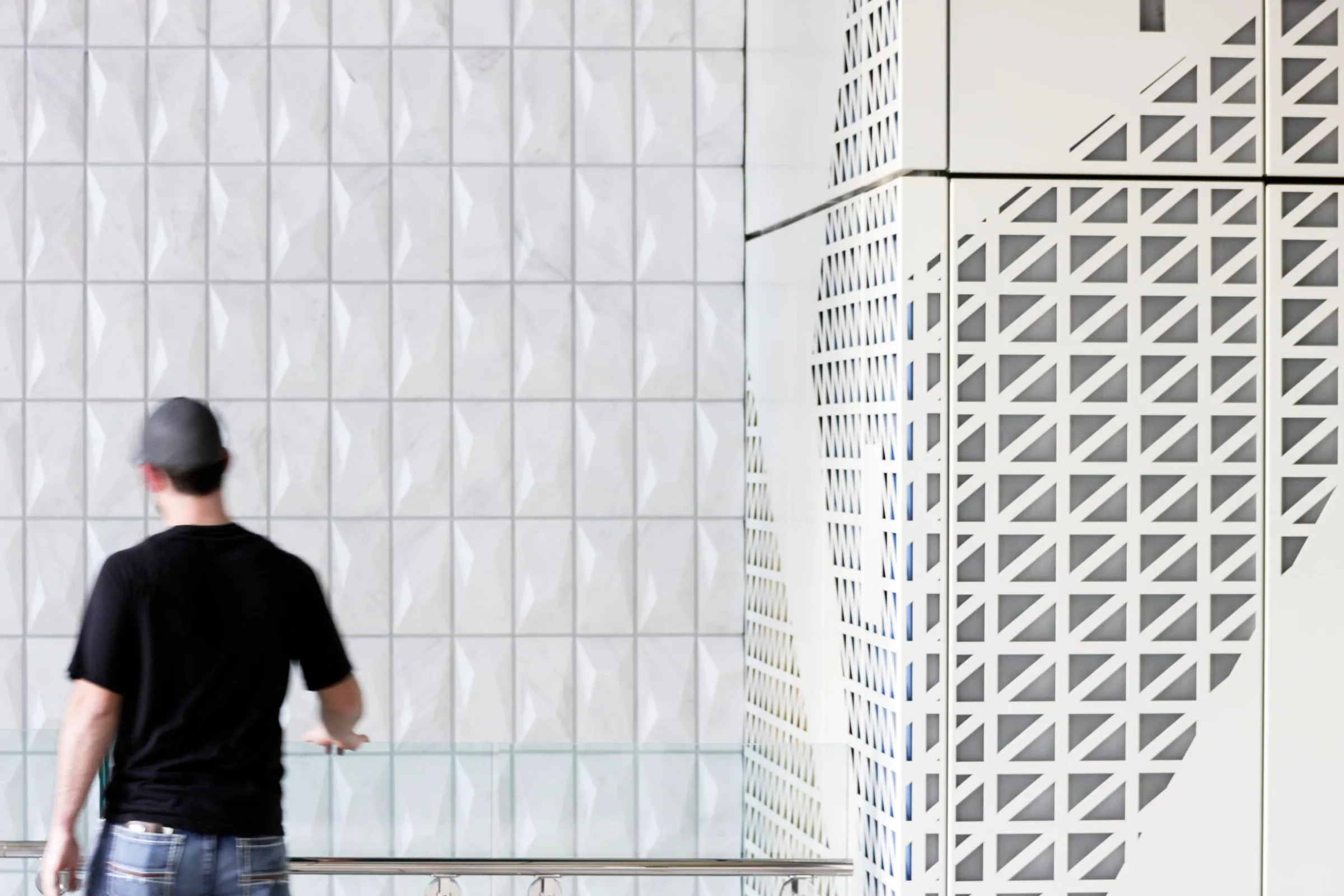 A man looking at a white wall of patterned metal tiles