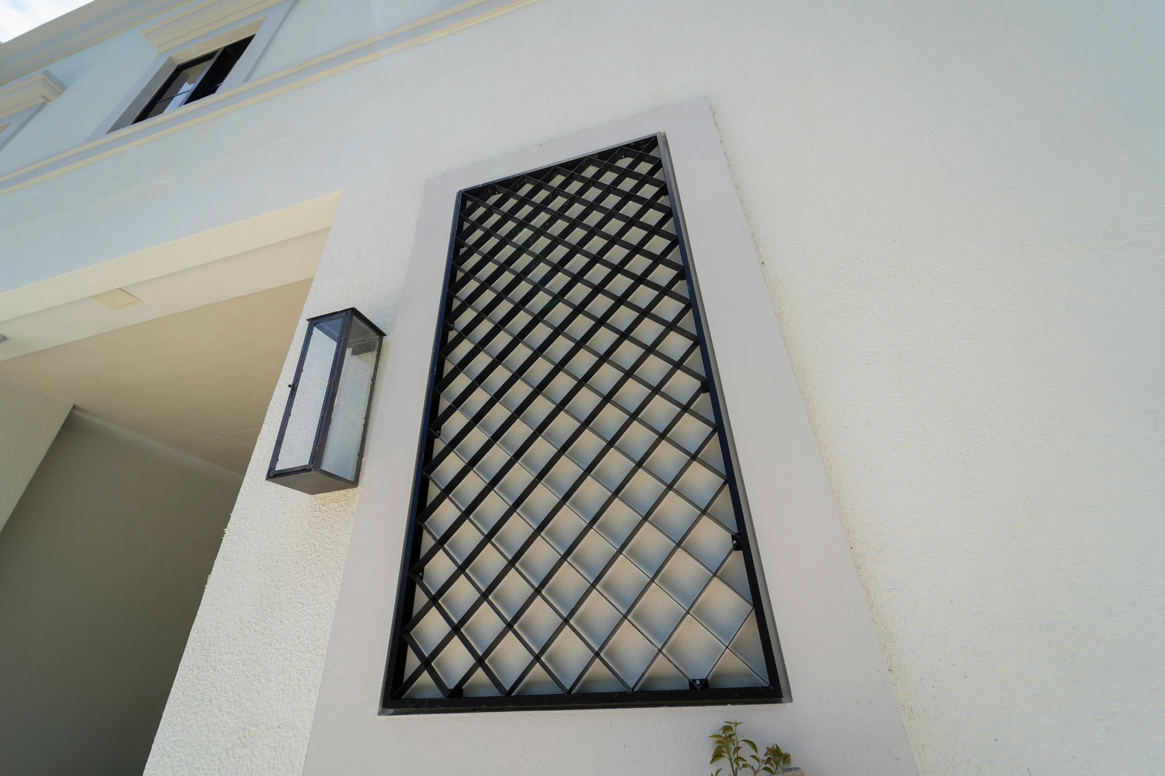 A lattice grille panel on a white wall beside a lantern