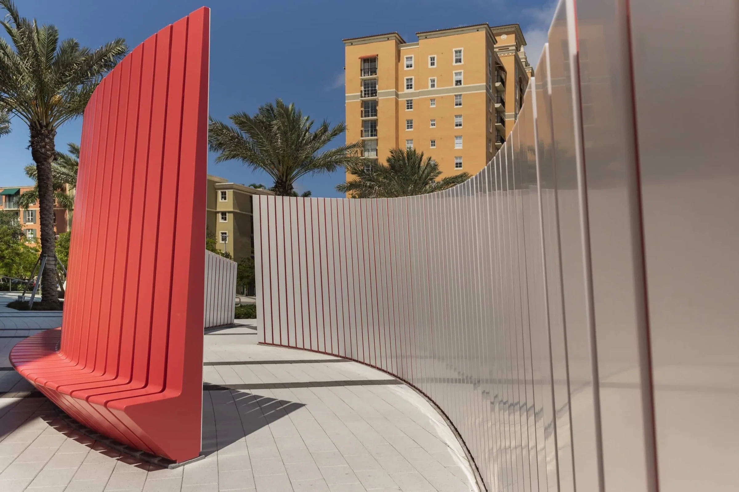 The tall red bench back curving away under palm trees
