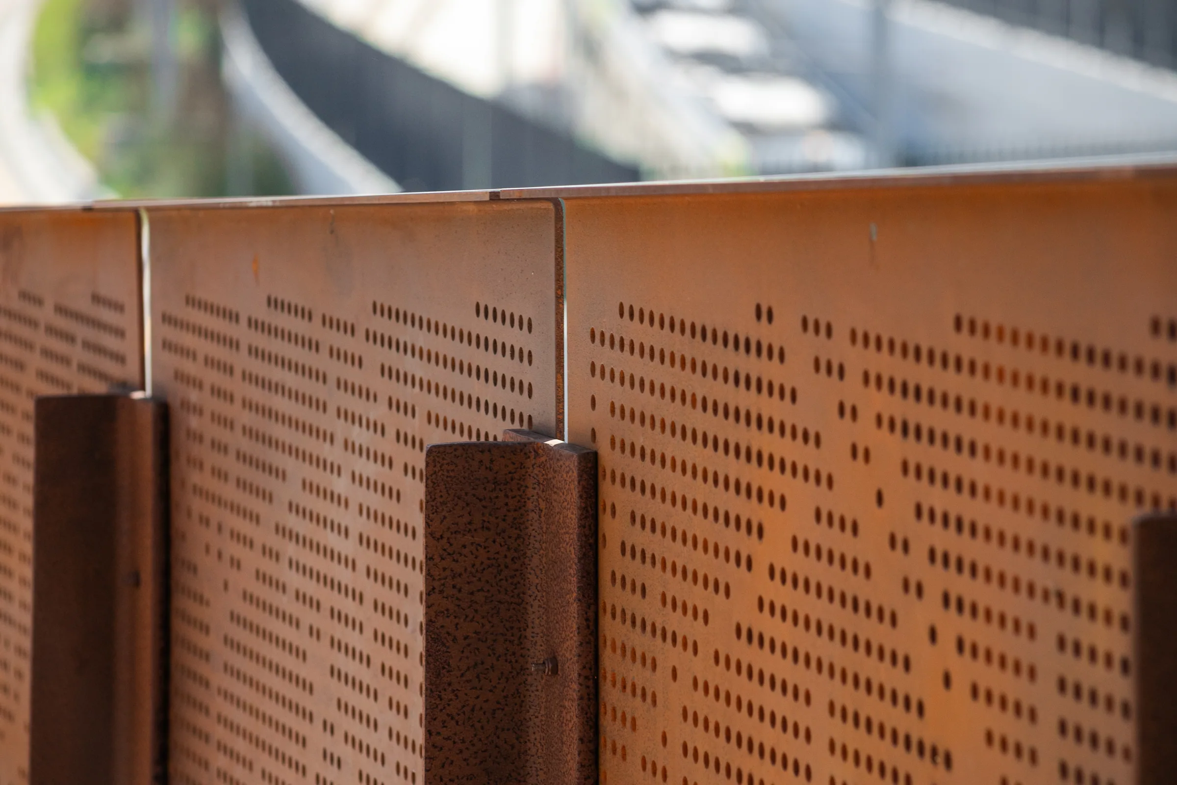 Perforated panels between steel posts, softly focused road behind