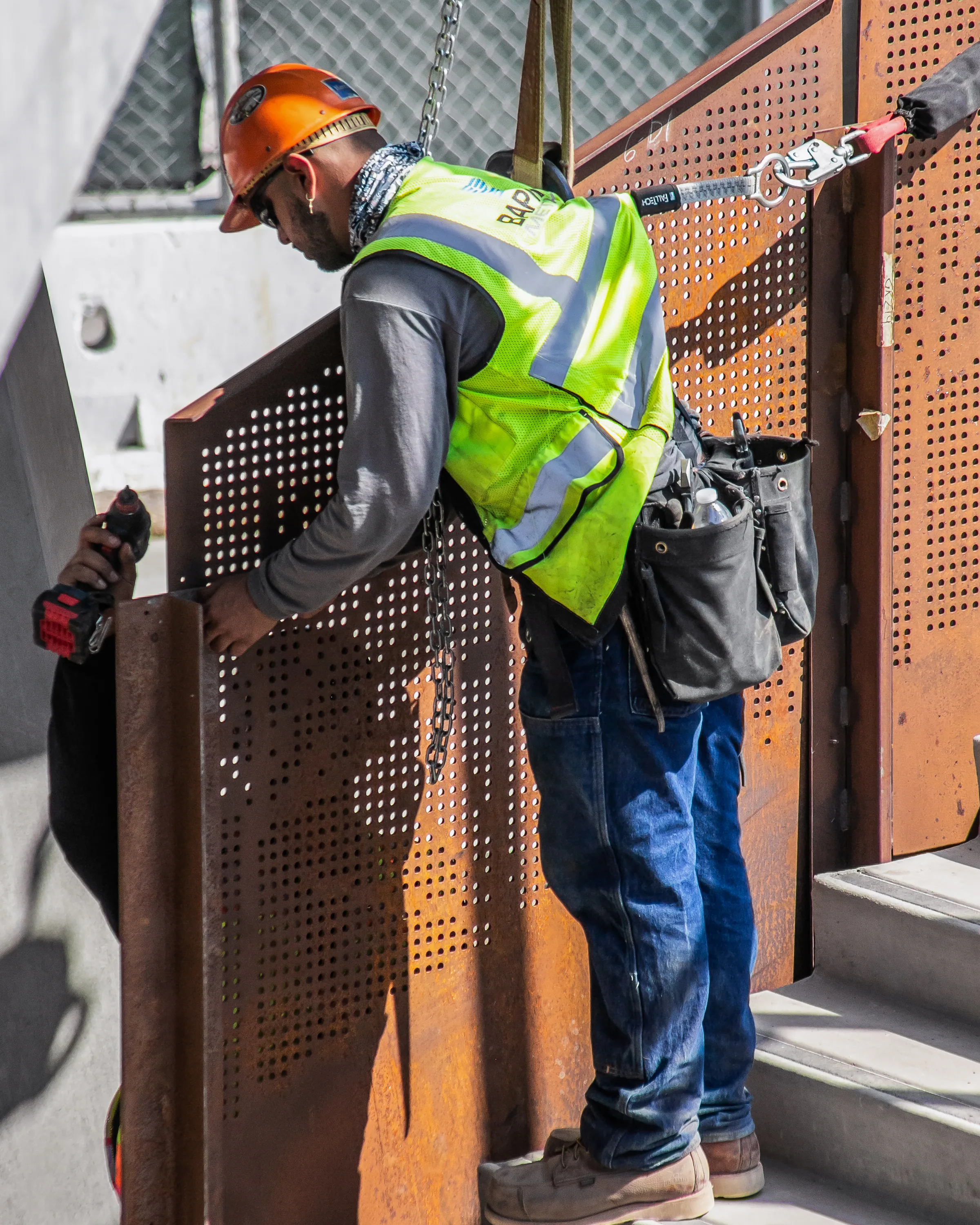 An installer in a safety vest bolting a perforated guard