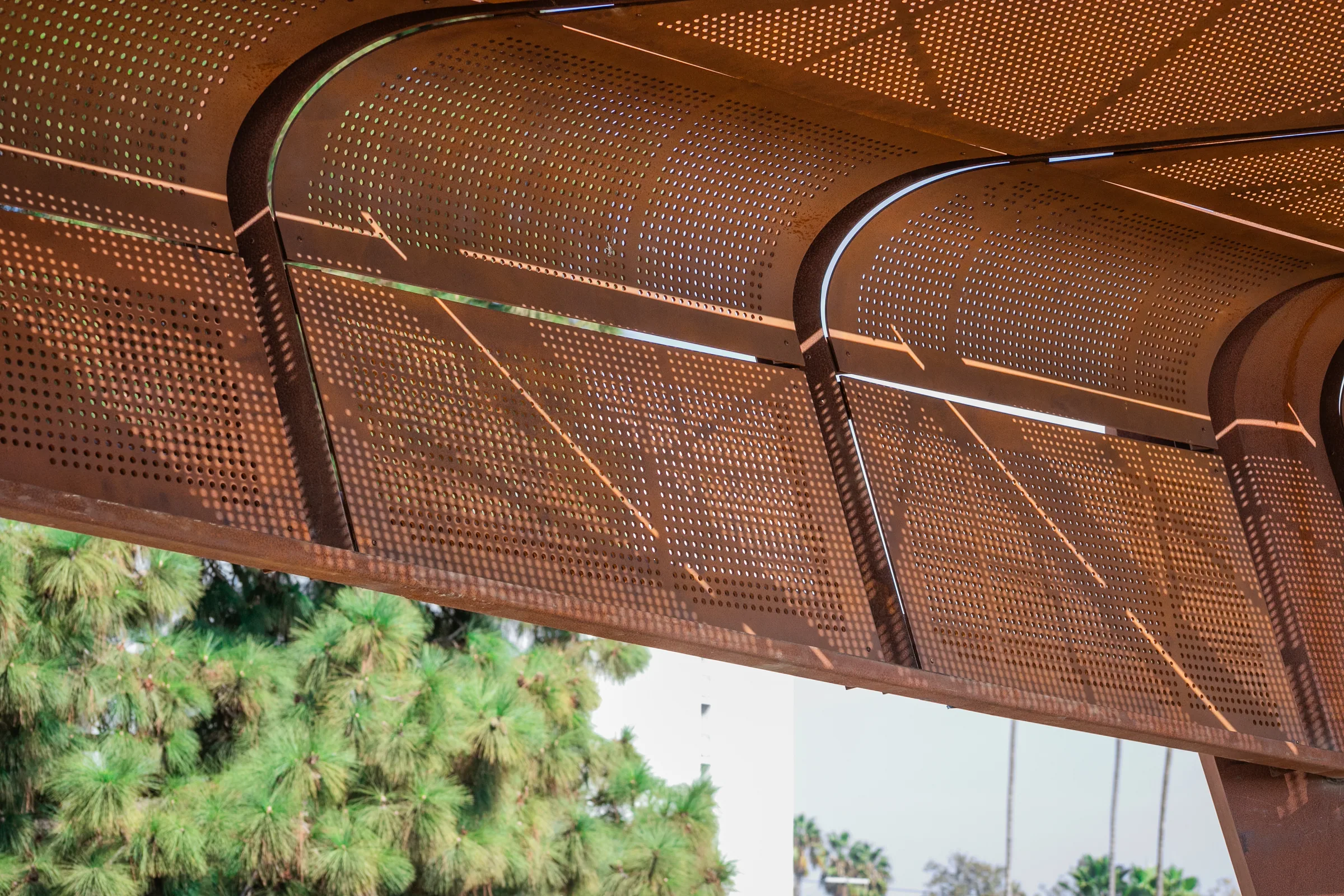 Rounded perforated panels along the canopy edge, trees behind