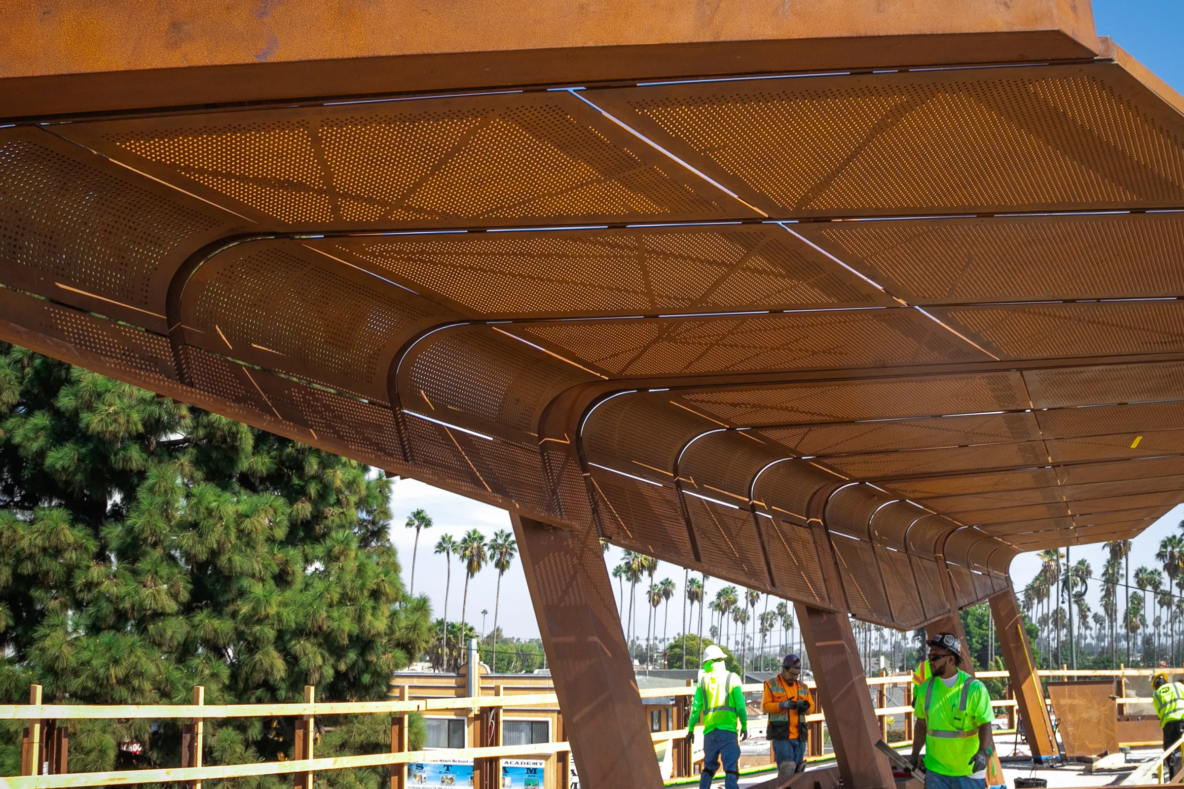 Under the curved steel canopy, palms and the work site beyond
