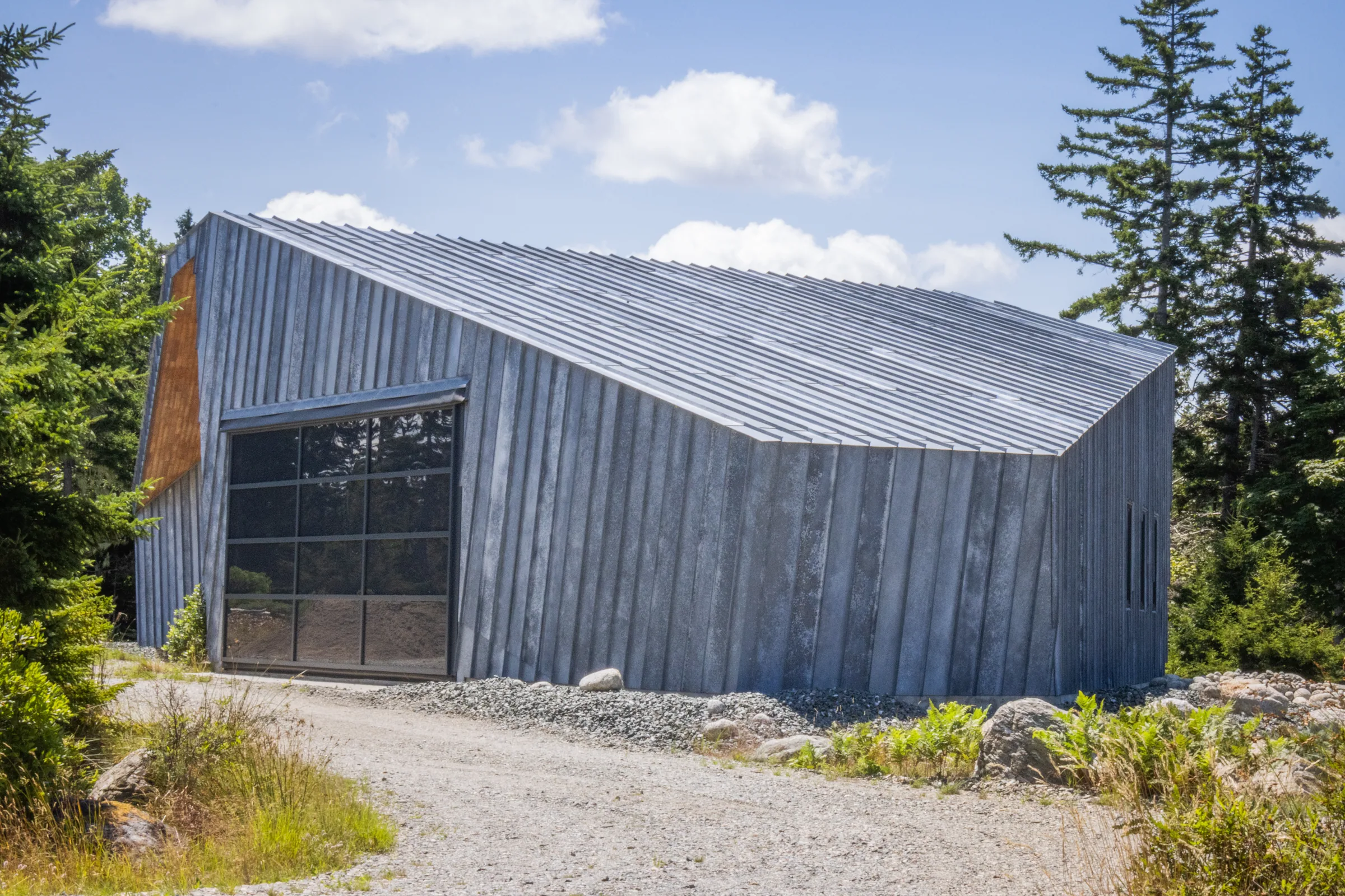 A zinc building with a large glazed door beside a gravel drive