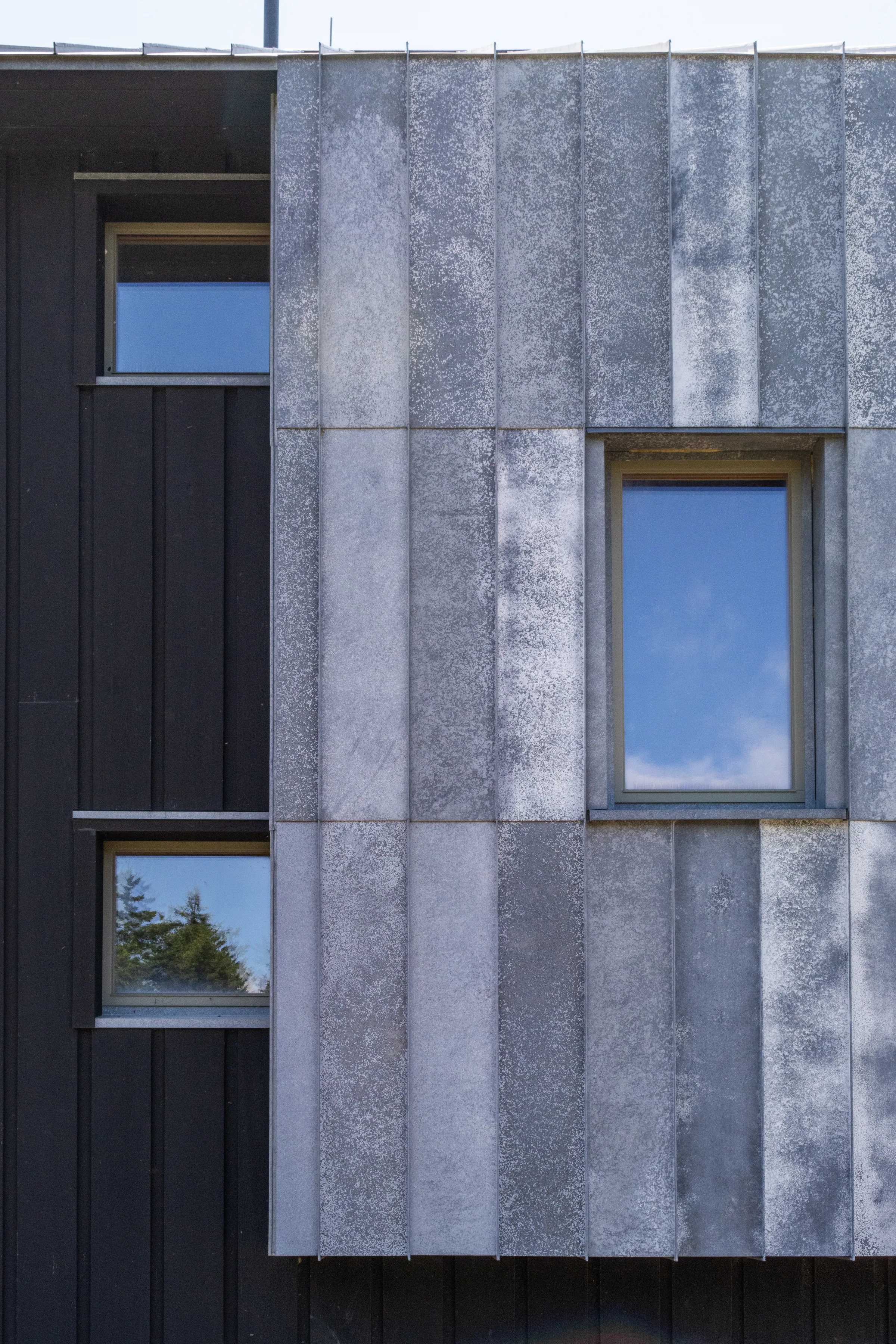 A narrow zinc bay with windows on a dark-clad house