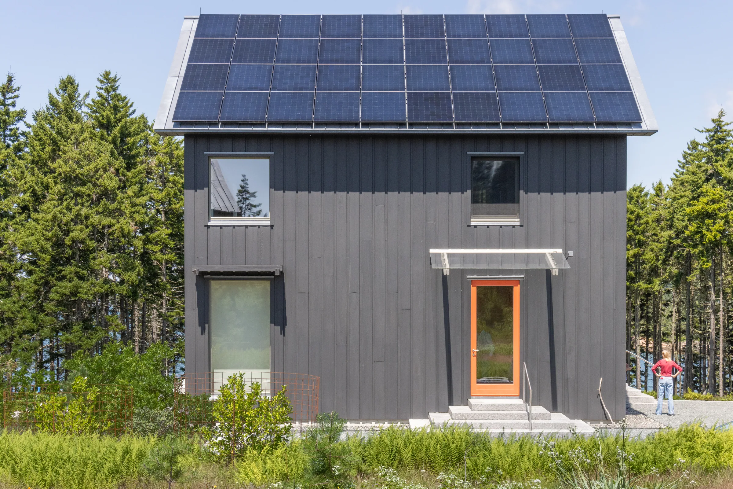 A dark board-clad house with solar panels on the roof
