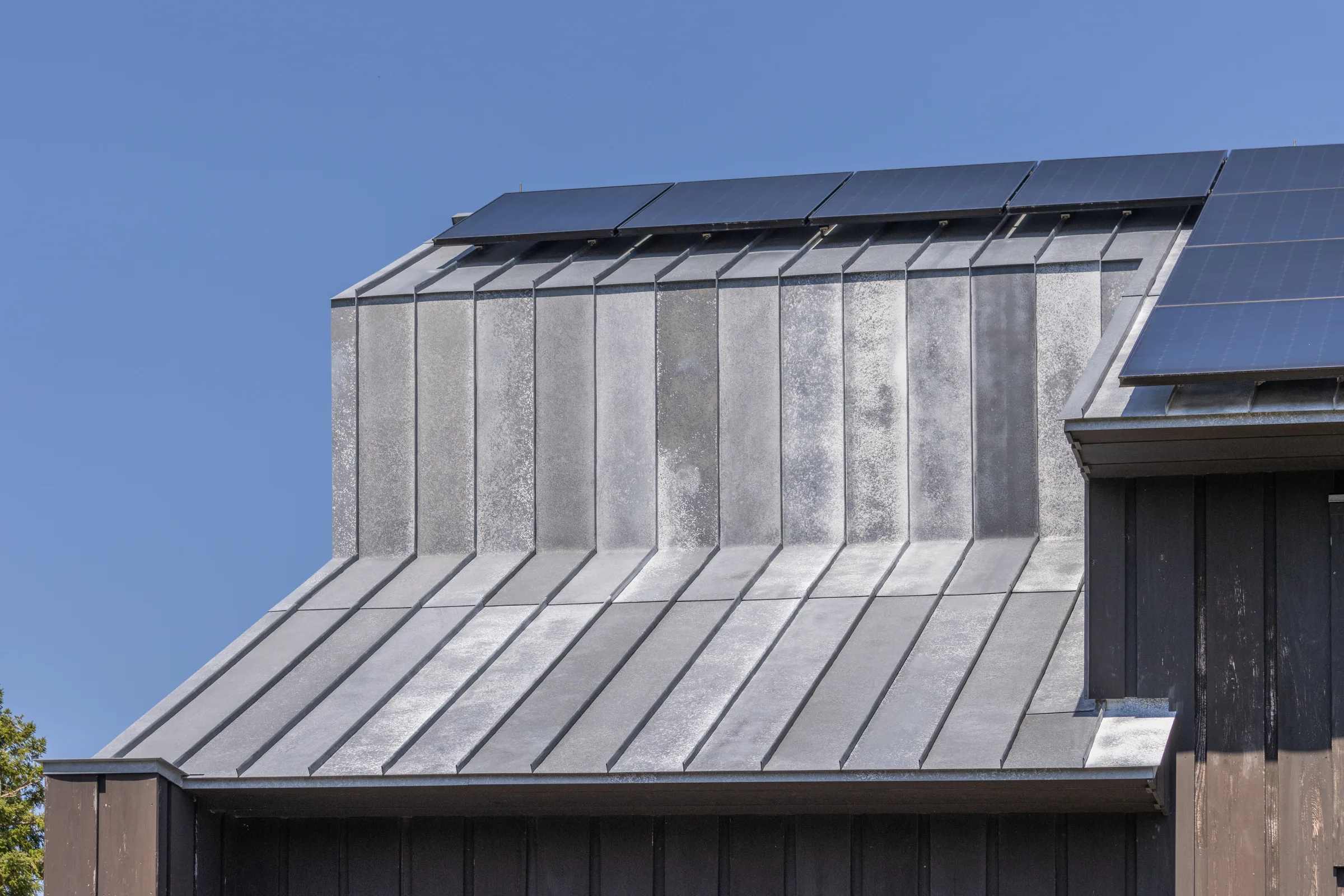 A zinc-clad addition meeting the dark house’s metal roof