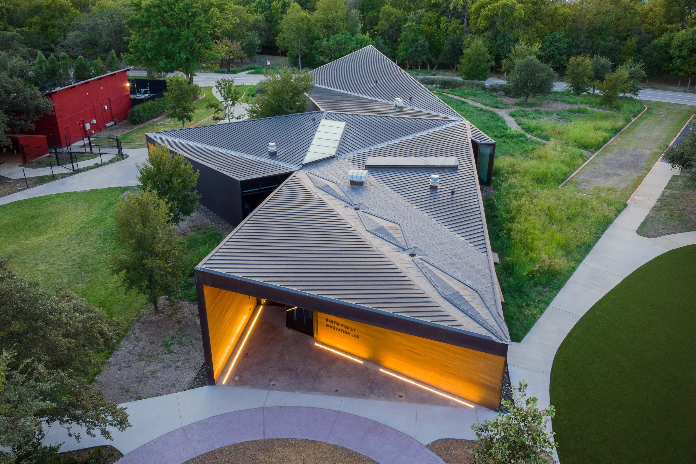 From above: folded copper roofs and a glowing entry beside a playing field