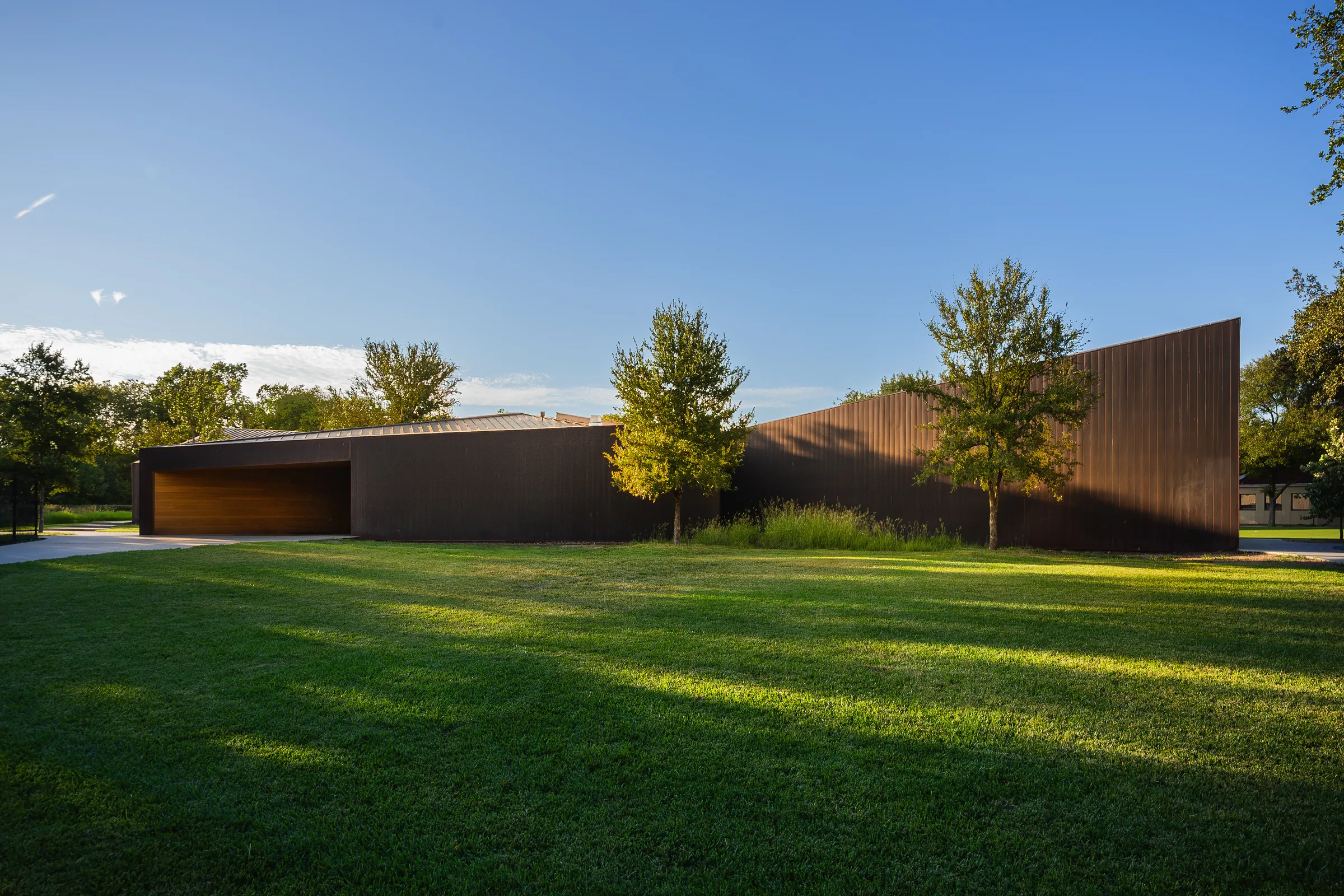 A low copper building across a lawn in the late sun