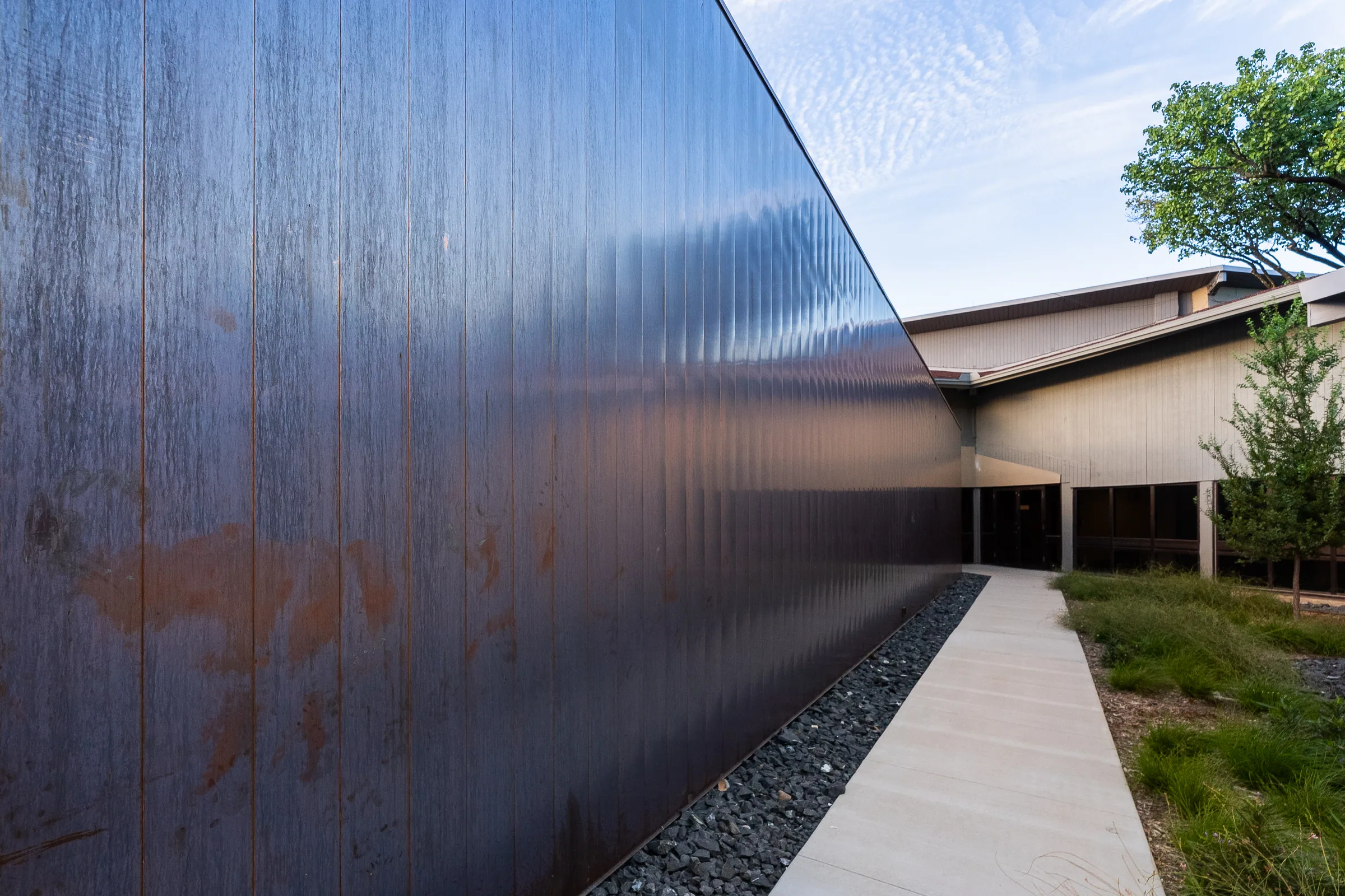A tall copper wall streaked with patina along a path