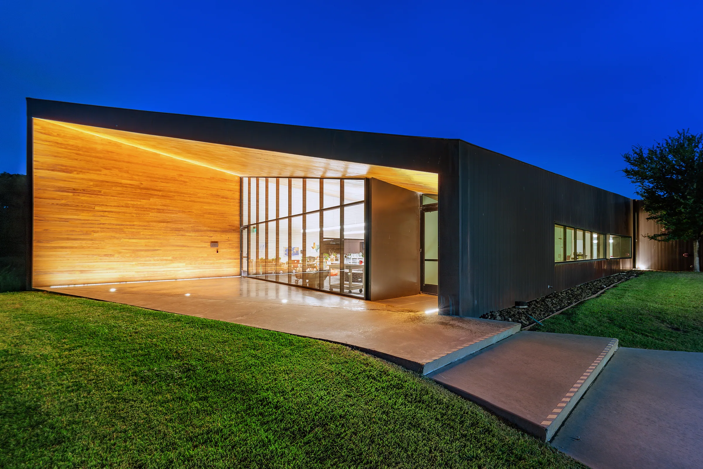 The lit wood soffit and glass end of a copper building at dusk