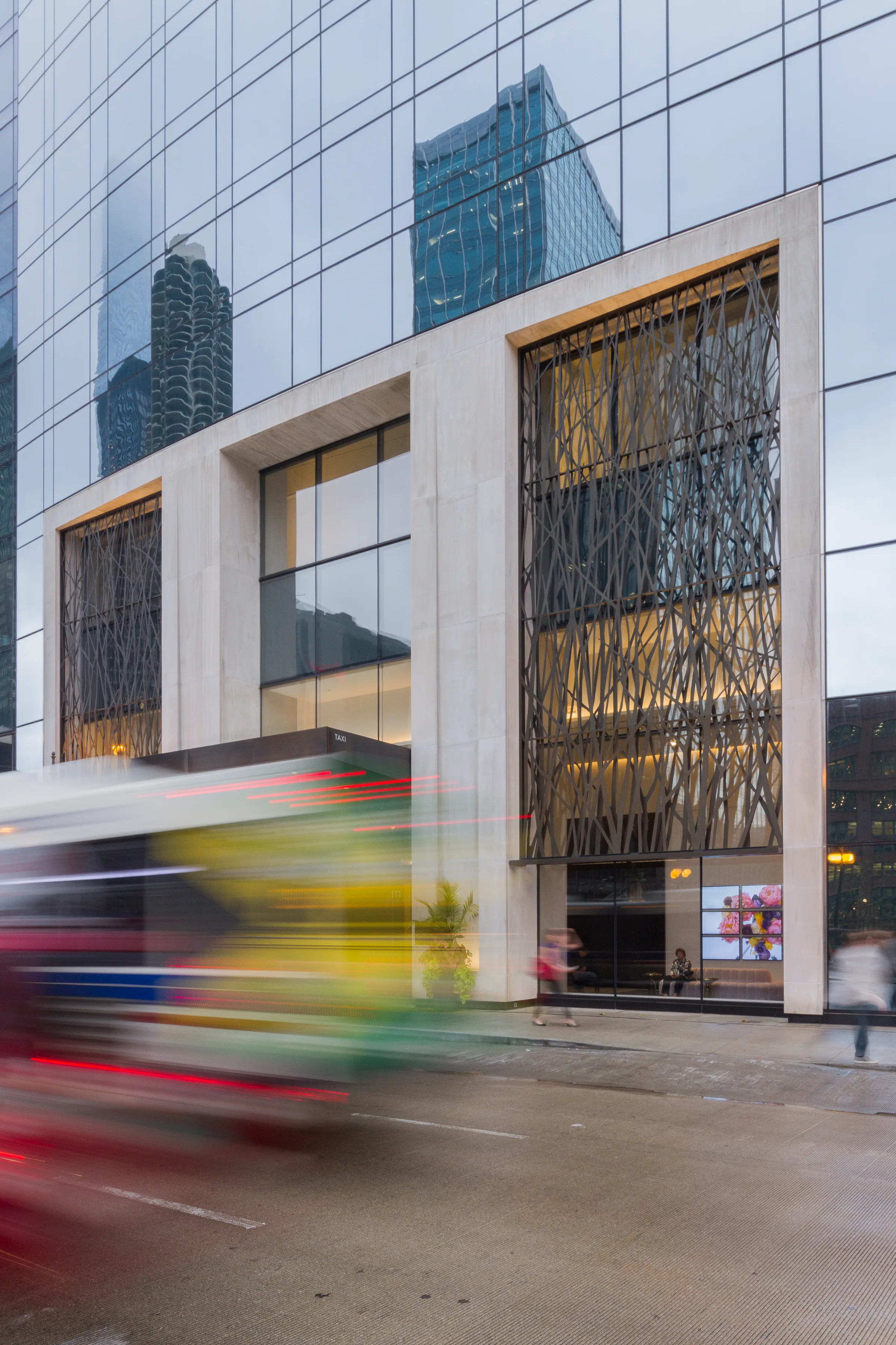 A bus blurs past the glowing perforated art wall below the glass tower