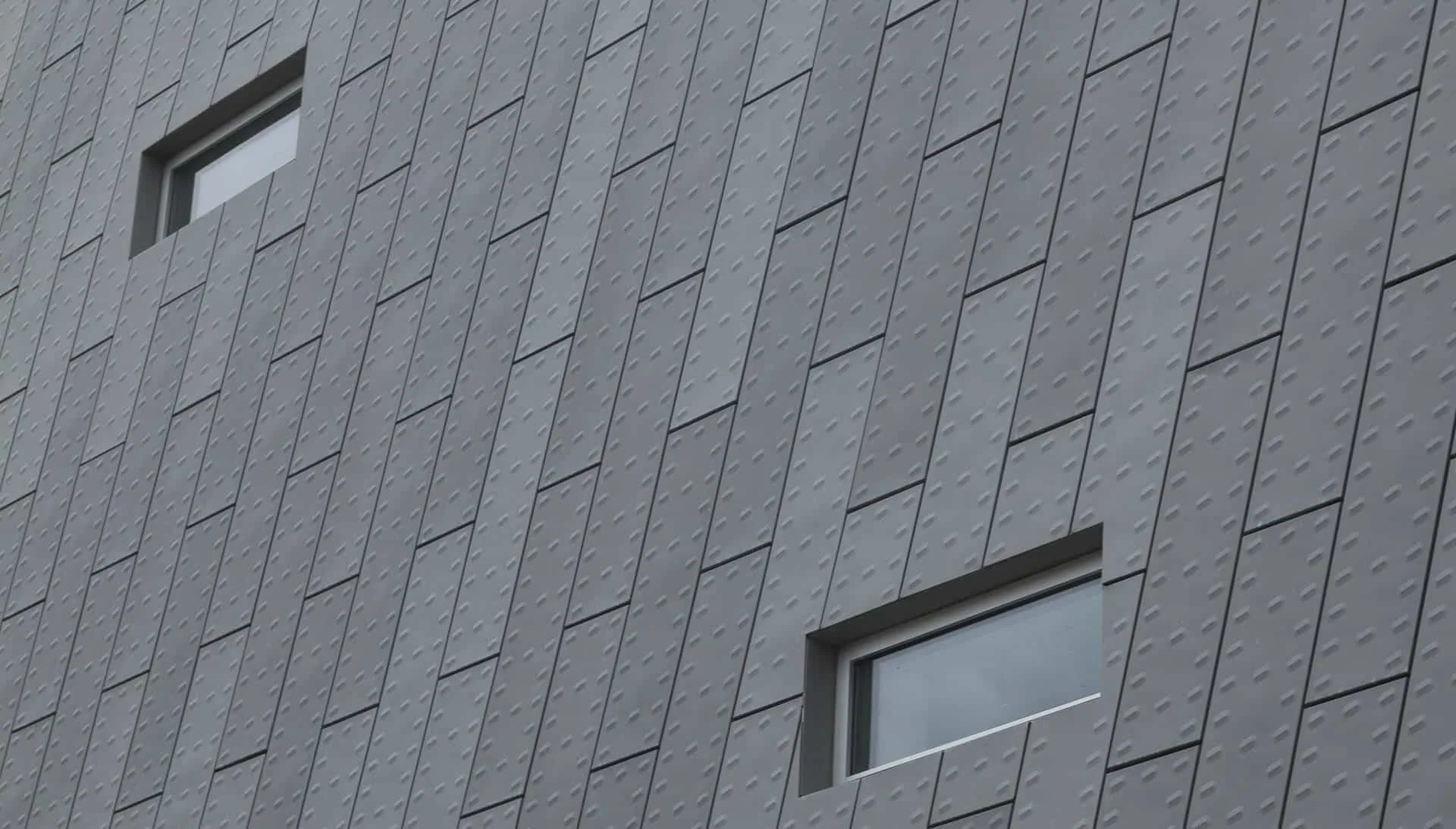 Punched windows in a zinc façade of embossed panels