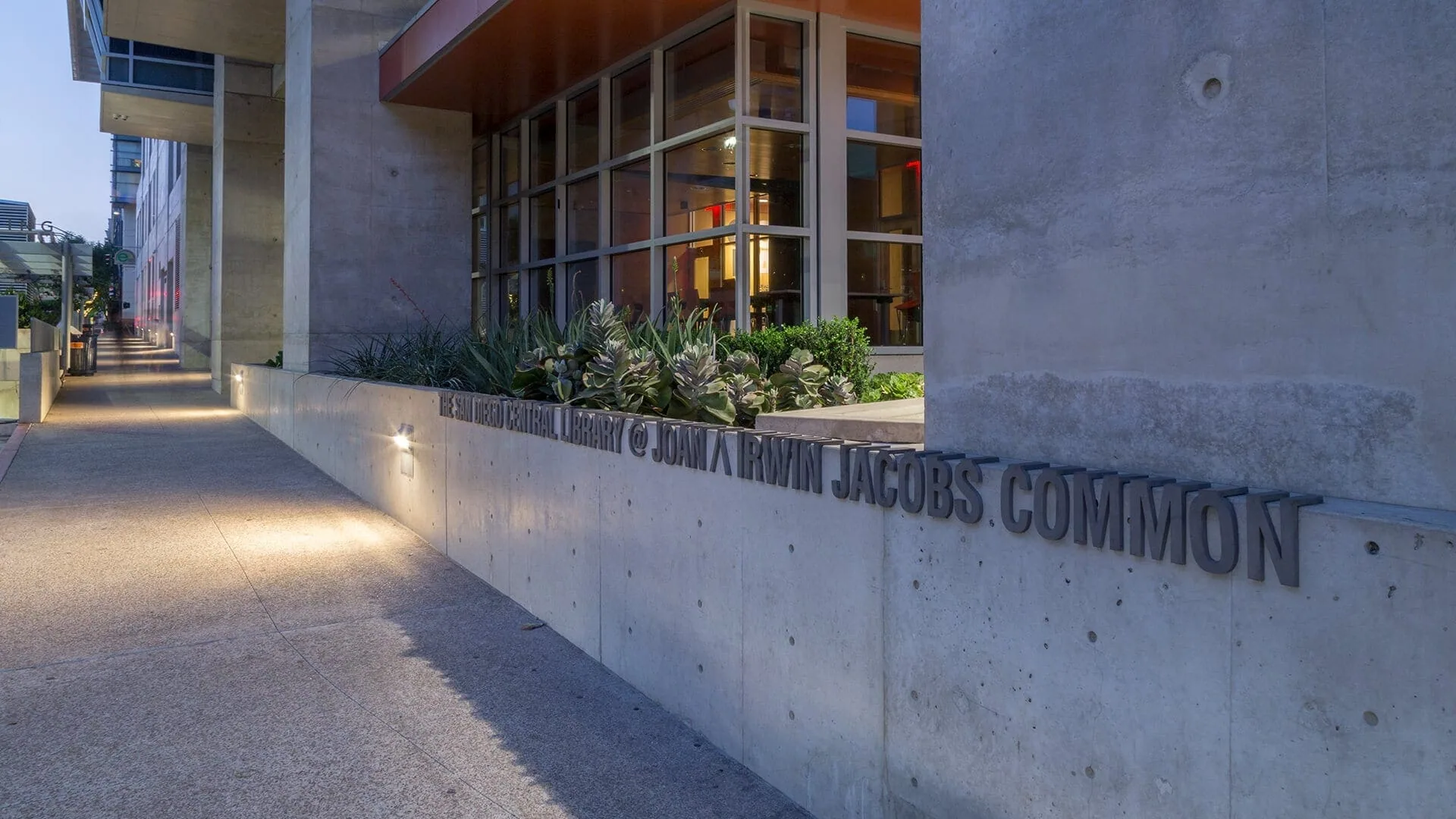 The lit Joan and Irwin Jacobs Common lettering along a walkway