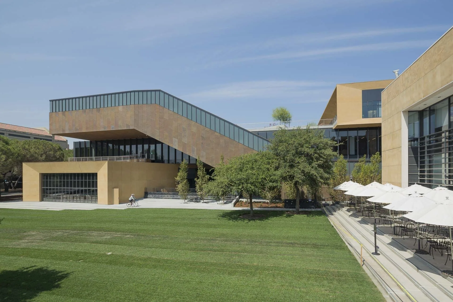 The building beyond a lawn and a terrace of umbrellas