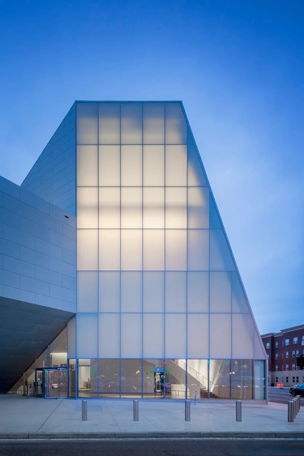 A glowing glass volume rising between zinc walls at twilight