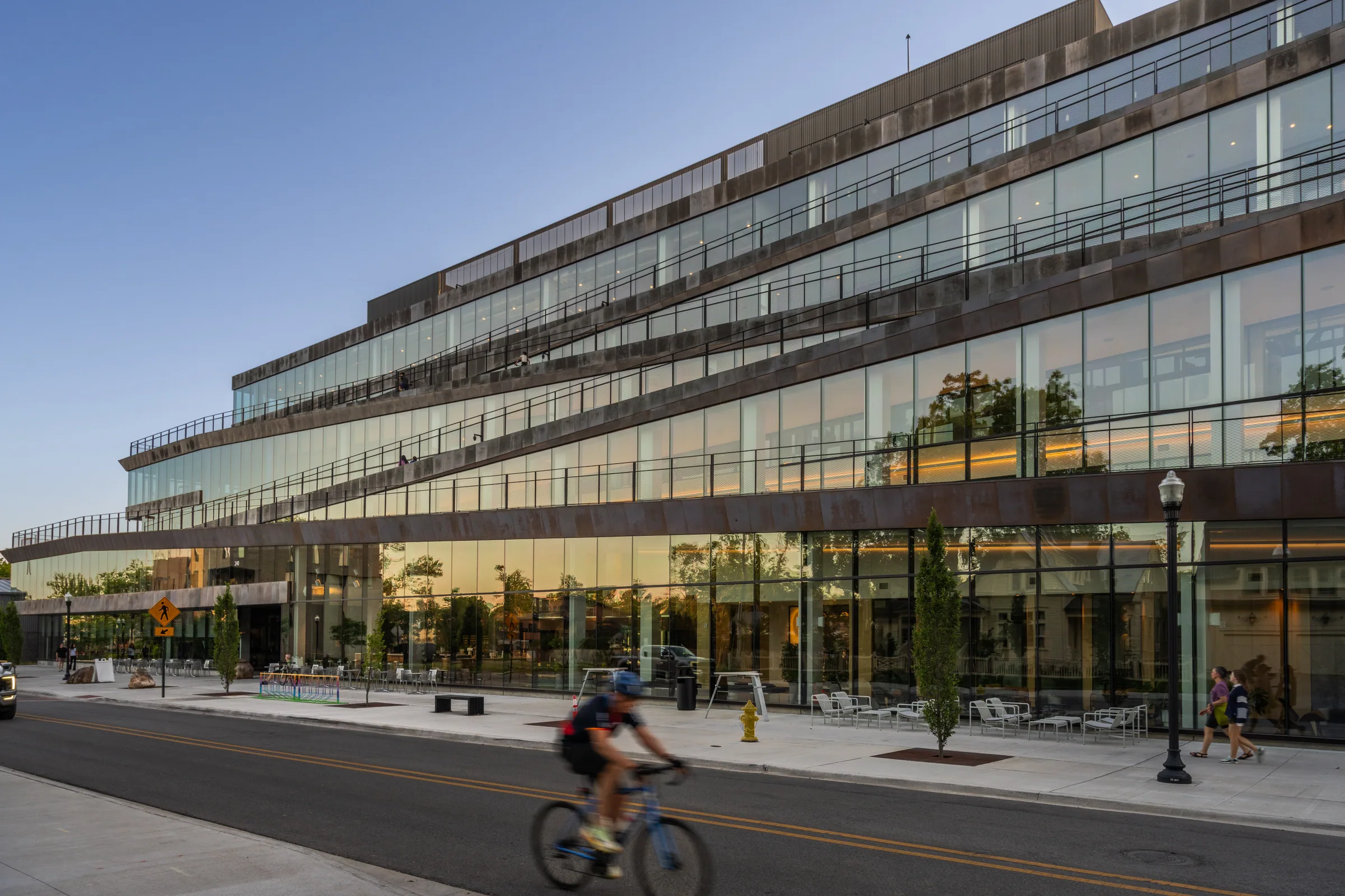 A cyclist passing the glass and copper front at sunset