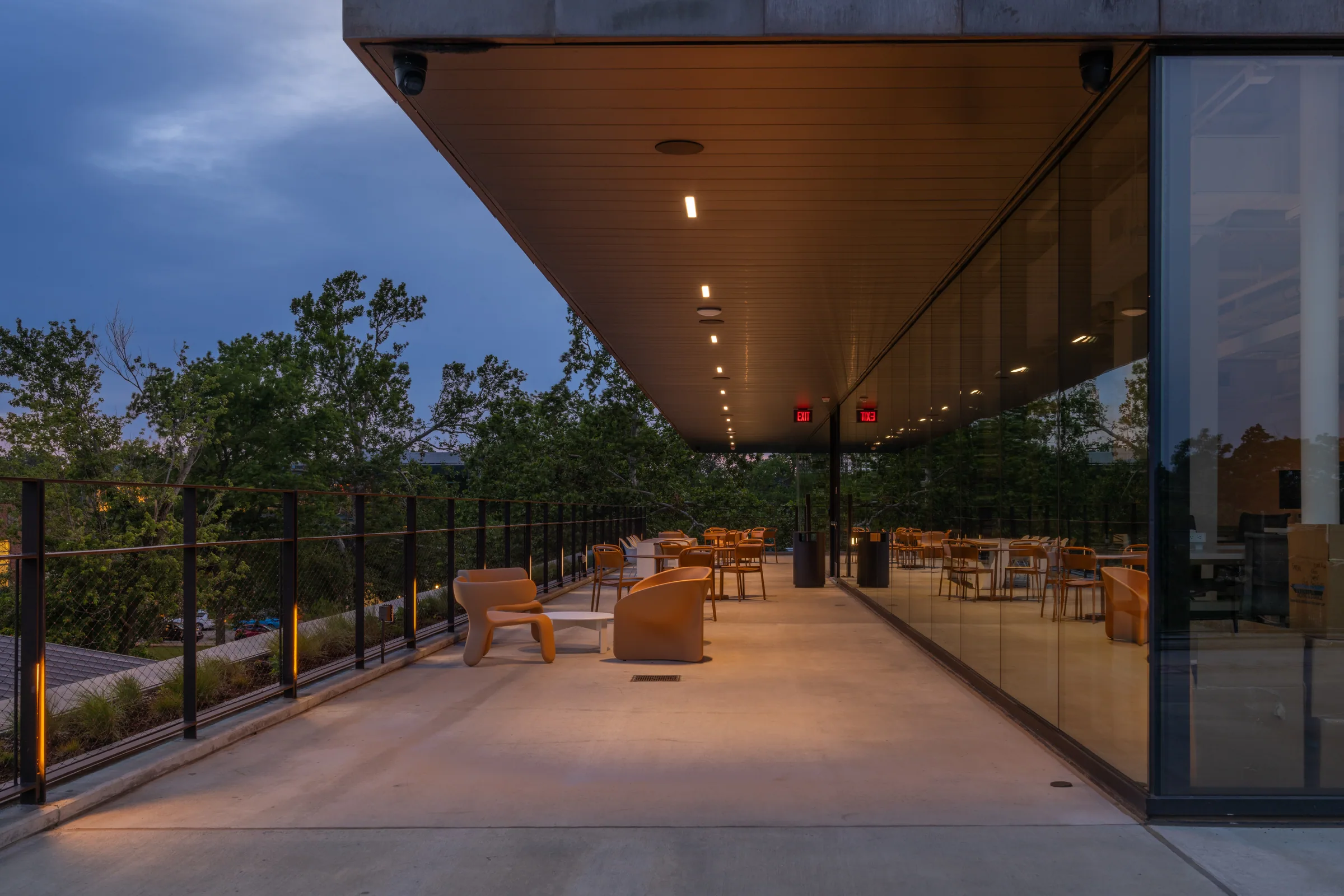 A covered terrace with chairs under a wood soffit at dusk